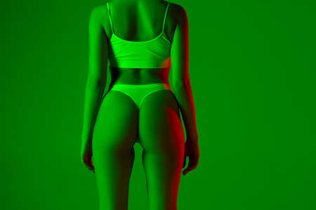 Fashion. Beautiful female back on green background in neon light. Beauty, cosmetics, spa, depilation, diet and treatment, fitness concept. Fit and sportive, sensual body with well-kept skin.の写真素材