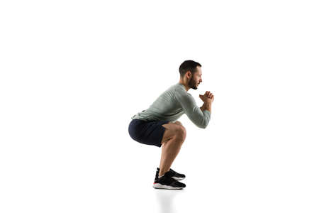 Squats. Young caucasian male model in action, motion on white background with copyspace. Concept of sport, movement, energy and dynamic, healthy lifestyle. Training, practicing. Authentic.の写真素材