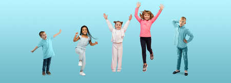 Group of elementary school kids or pupils jumping in colorful casual clothes on blue studio...