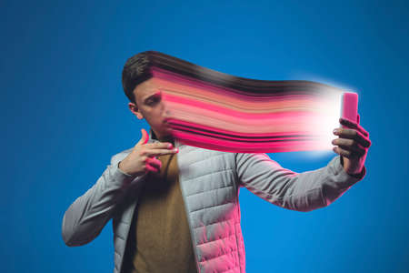 Cinematic portrait of stylish man in neon lighted interior using a smartphone. The face is smeared, sucked, absorbed into the phone. Concept of social network dependency, phone addiction.の写真素材