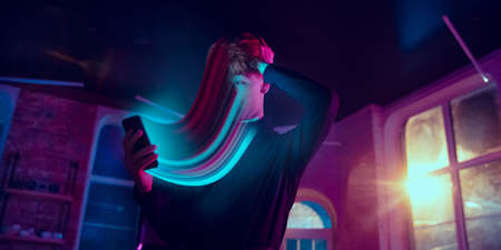 Cinematic portrait of stylish man in neon lighted interior using a smartphone. The face is smeared,...