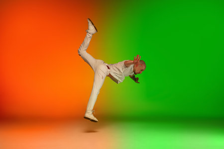 Flying. Stylish sportive caucasian man dancing hip-hop on colorful gradient background at dance hall...