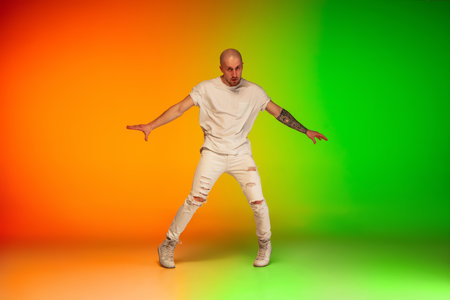 Urban. Stylish sportive caucasian man dancing hip-hop on colorful gradient background at dance hall in neon light. Youth culture, movement, style and fashion, action. Fashionable bright portrait.の写真素材