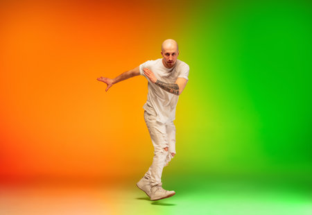 Fire. Stylish sportive caucasian man dancing hip-hop on colorful gradient background at dance hall in neon light. Youth culture, movement, style and fashion, action. Fashionable bright portrait.の写真素材