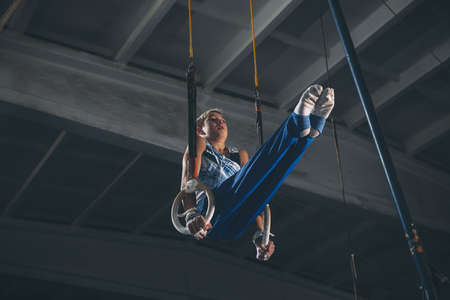 Flying. Little male gymnast training in gym, composed and active. Caucasian fit boy, athlete in sportswear practicing in exercises for strength, balance. Movement, action, motion, dynamic conceptの写真素材