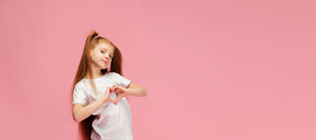 Heart with hands, flyer. Happy, smiley little caucasian girl isolated on pink studio background with copyspace for ad. Looks happy. Childhood, education, human emotions, facial expression concept.の写真素材