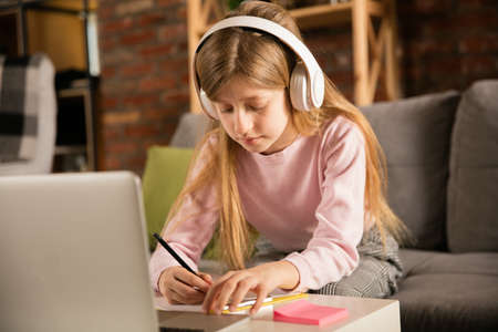 Little girl studying by group video call, use video conference with teacher, listening to online course. Using headphones, notebook. Easy, comfortable usage concept, education, online, childhood.の写真素材