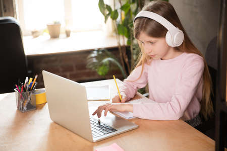 Little girl studying by group video call, use video conference with teacher, listening to online course. Using headphones, notebook. Easy, comfortable usage concept, education, online, childhood.の写真素材