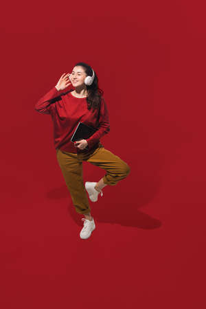 Dancing with headphones. High angle view of young woman on red studio background. Human emotions and...