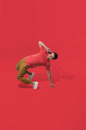 Talking phone. High angle view of young man on red studio background. Boy in motion. Human emotions and facial expressions concept. Full length portait, copyspace for ad. Fashion, retro style.の写真素材