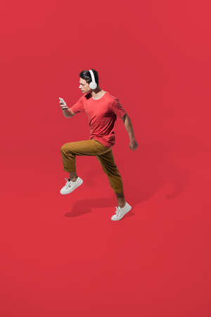Listening to music on the go. High angle view of young man on red background. Boy in motion. Human...