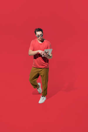 Scrolling tablet on the go. High angle view of young man on red background. Boy in motion. Human...