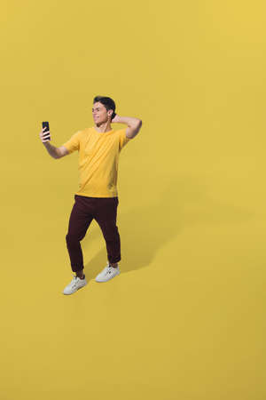 Taking selfie on the go. High angle view of young man on yellow background. Boy in motion. Human...