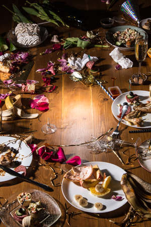 Early morning after the party. Glasses and plates on the table with confetti and serpentine, leftovers, flower petals. Food, drink, afterparty, hangover, celebration and lifestyle concept. Copyspace.の写真素材