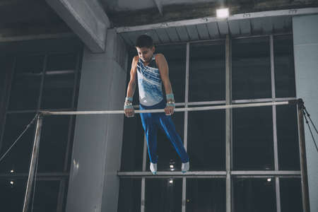 Little male gymnast training in gym, flexible and active. Caucasian fit little boy, athlete in sportswear practicing in exercises for strength, balance.の写真素材