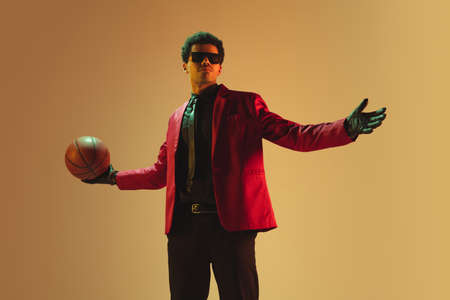 High-fashion styled man in red jacket playing basketball isolated over brown backgroundの写真素材