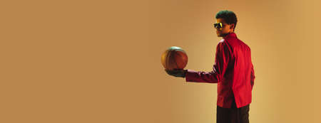 High-fashion styled man in red jacket playing basketball isolated over brown backgroundの写真素材