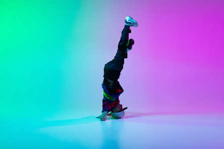 Beautiful sportive boy dancing hip-hop in stylish clothes on colorful gradient background at dance hall in neon light.の写真素材