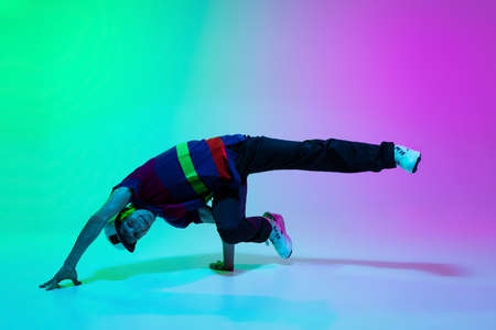 Beautiful sportive boy dancing hip-hop in stylish clothes on colorful gradient background at dance hall in neon light.の写真素材