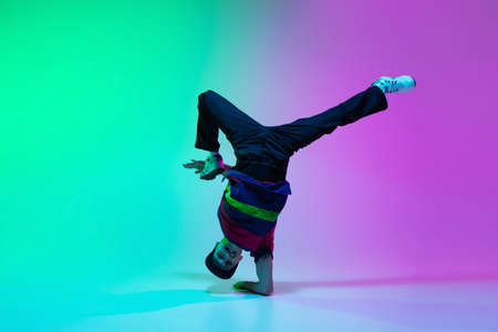 Beautiful sportive boy dancing hip-hop in stylish clothes on colorful gradient background at dance hall in neon light.の写真素材