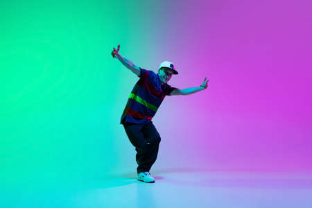 Beautiful sportive boy dancing hip-hop in stylish clothes on colorful gradient background at dance hall in neon light.の写真素材