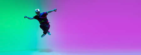 Beautiful sportive boy dancing hip-hop in stylish clothes on colorful gradient background at dance hall in neon light.の写真素材