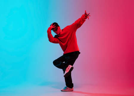 Beautiful sportive boy dancing hip-hop in stylish clothes on colorful gradient background at dance hall in neon light.の写真素材