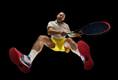 Young caucasian tennis player in action, motion isolated on black background, look from the bottom. Concept of sport, movement, energy and dynamic.の写真素材