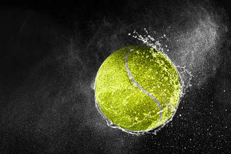Tennis ball flying in water drops and splashes isolated on black backgroundの写真素材