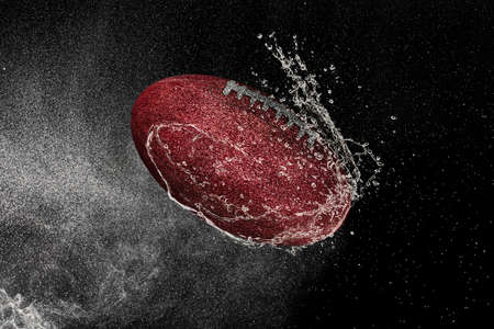 American football ball flying in water drops and splashes isolated on black backgroundの写真素材