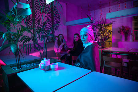 Beautiful girl with a pearl earring taking lunch in modern cafe, restaurant in neon lightの写真素材