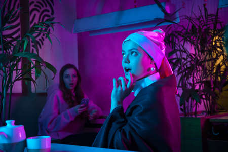 Beautiful girl with a pearl earring taking lunch in modern cafe, restaurant in neon lightの写真素材