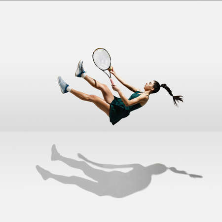 Young caucasian professional sportswoman levitating, flying while playing tennis isolated on white backgroundの写真素材
