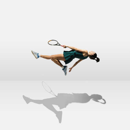 Young caucasian professional sportswoman levitating, flying while playing tennis isolated on white backgroundの写真素材