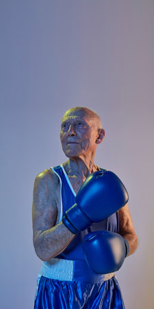 Senior man wearing sportwear boxing isolated on gradient studio background in neon light. Concept of sport, activity, movement, wellbeing. Copyspace, ad.の写真素材