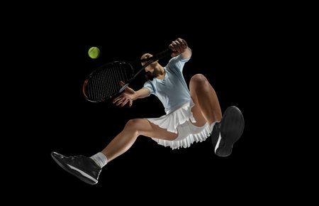 Move. Female professional tennis player in action, motion isolated on black background, look from the bottom. Concept of sport, movement, energy and dynamic, healthy lifestyle. Training, practicing.の写真素材