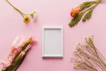 Flowers and white frame on coral pink background. Greeting card to Mother's, Parent's day. Beautiful floral mock up with copyspace. Celebrating, spring and summer mood, family concept. Feminine look.の写真素材