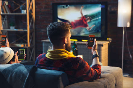 Group of friends watching TV, sport match together. Emotional fans cheering for favorite team, watching exciting football. Concept of friendship, leisure activity, emotions. Betting, finance, fun.の写真素材