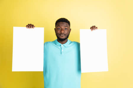 Young African man with blank sheets of paper isolated over yellow studio background.の写真素材