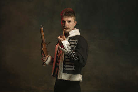 Young man in suit as royal person isolated on dark green background. Retro style, comparison of eras concept. Beautiful male model like historical character, monarch, old-fashioned.の写真素材