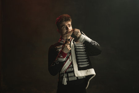 Young man in suit as royal person isolated on dark green background. Retro style, comparison of eras concept. Beautiful male model like historical character, monarch, old-fashioned.の写真素材