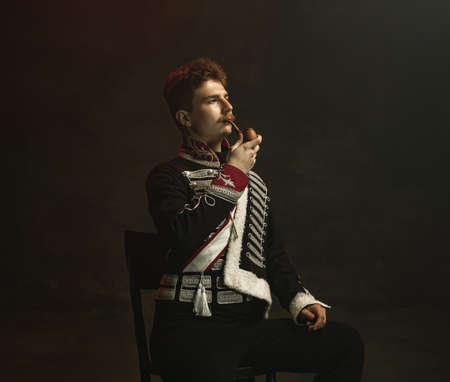 Young man in suit as royal person isolated on dark green background. Retro style, comparison of eras concept. Beautiful male model like historical character, monarch, old-fashioned.の写真素材