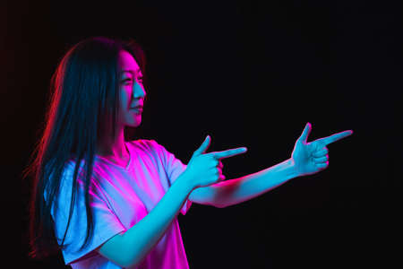 Asian young womans portrait on dark studio background in neon. Concept of human emotions, facial expression, youth, sales, ad.の写真素材