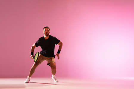 Young caucasian man playing tennis isolated on pink studio background, action and motion concept