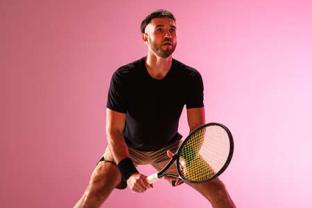 Young caucasian man playing tennis isolated on pink studio background, action and motion conceptの写真素材