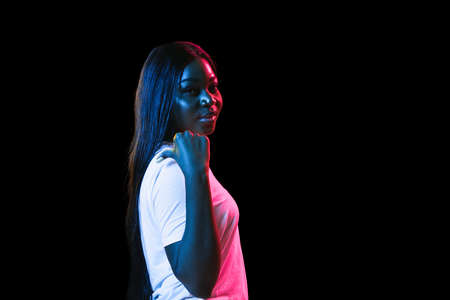 African young womans portrait on dark studio background in neon. Concept of human emotions, facial...