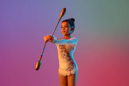 African-american rhythmic gymnast, pretty girl practicing on gradient studio background in neon...
