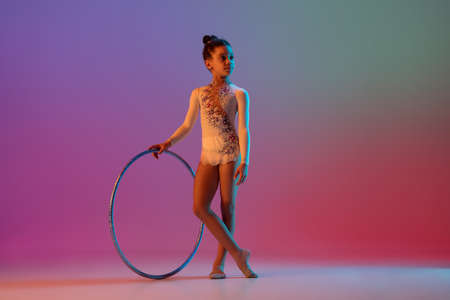 African-american rhythmic gymnast, pretty girl practicing on gradient studio background in neon lightの写真素材