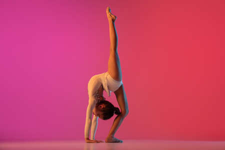 African-american rhythmic gymnast, pretty girl practicing on gradient studio background in neon...