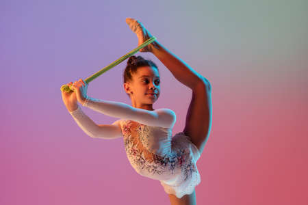 African-american rhythmic gymnast, pretty girl practicing on gradient studio background in neon...
